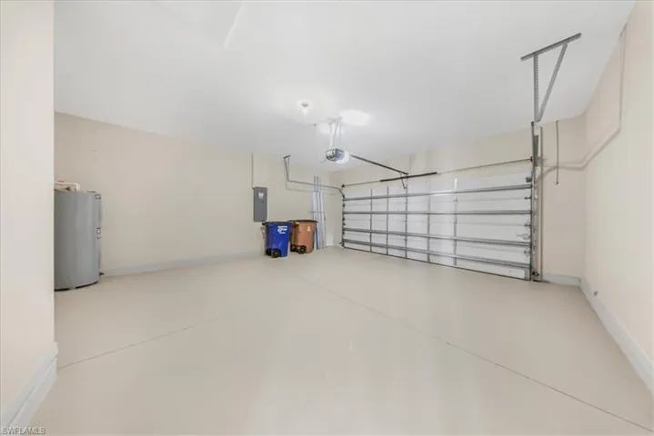 Garage with electric water heater, electric panel, and a garage door opener