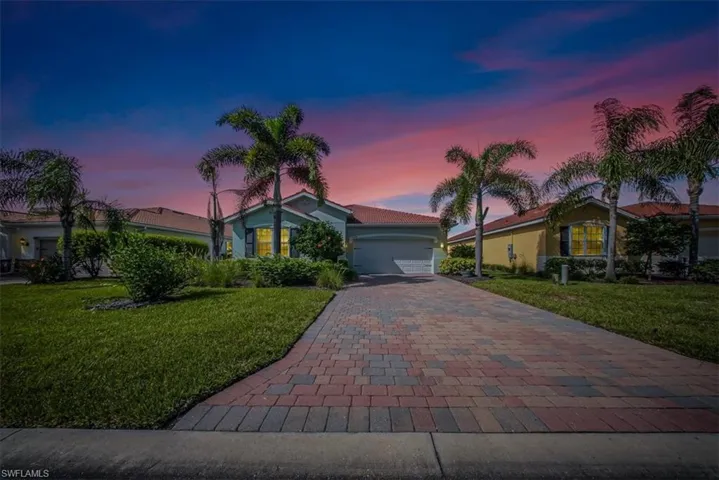 View of front facade with a yard, a garage, decorative driveway, and stucco siding
