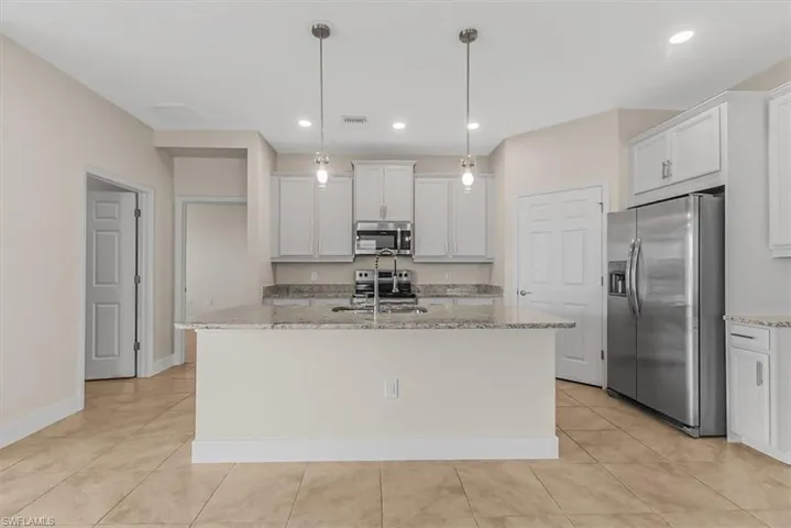 Kitchen featuring appliances with stainless steel finishes, light stone countertops, pendant lighting, white cabinetry, and a kitchen island with sink