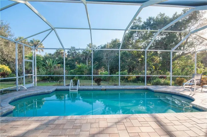 Outdoor pool surrounded by nature featuring a sunroom, screened enclosure, and a patio area