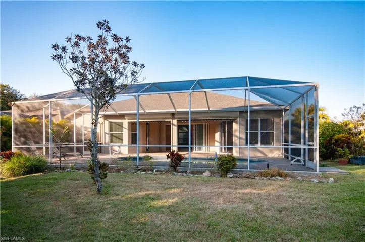 Back of house with a sunroom, an outdoor pool, screened  enclosure, and a lawn