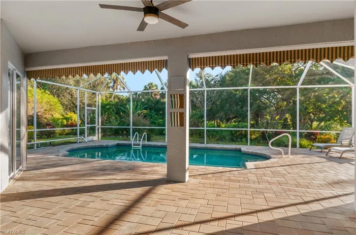 Swimming pool with a sunroom, a patio, glass enclosure, view of scattered trees, and a ceiling fan