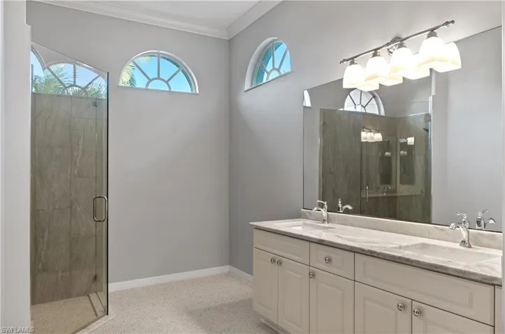 Bathroom with double vanity, a shower stall, and crown molding