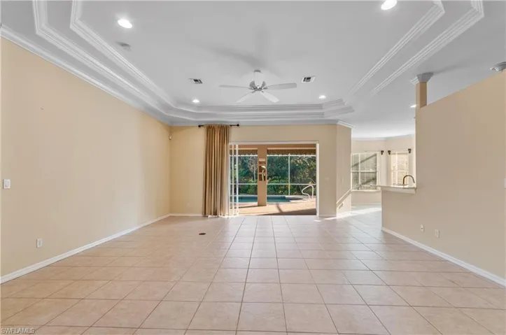 Great room with ornamental crown molding, light tile patterned floors, ceiling fan, recessed lighting, and a tray ceiling