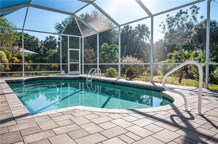 Swimming pool with screened enclosure, view lush trees and shrubs, and a sunroom