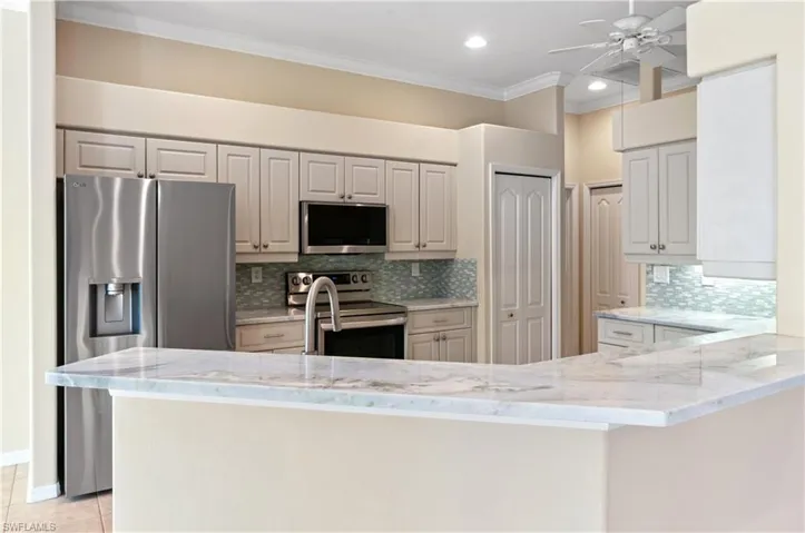 Kitchen with light stone counters, appliances with stainless steel finishes, ornamental molding, a peninsula, and decorative backsplash