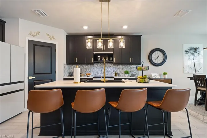 Kitchen with decorative light fixtures, backsplash, a kitchen island with sink, a kitchen bar, and recessed lighting