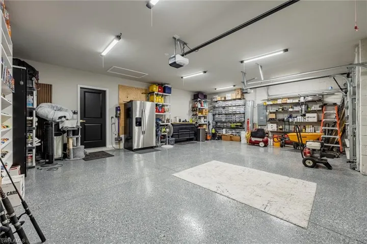 Garage featuring stainless steel fridge, a workshop area, electric panel, and a garage door opener