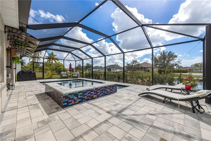 Outdoor pool featuring glass enclosure, an in-ground hot tub, a sunroom, and area for grilling