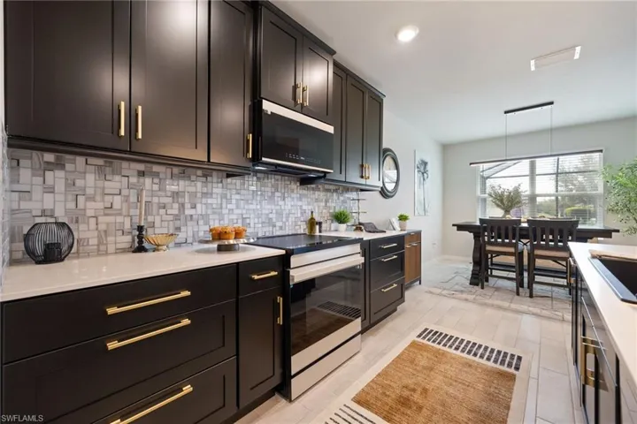 Kitchen featuring electric stove, decorative backsplash, decorative light fixtures, stainless steel microwave, and light stone counters