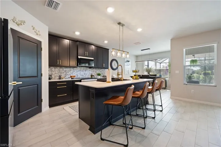 Kitchen with backsplash, hanging light fixtures, a kitchen island with sink, a breakfast bar area, and freestanding refrigerator