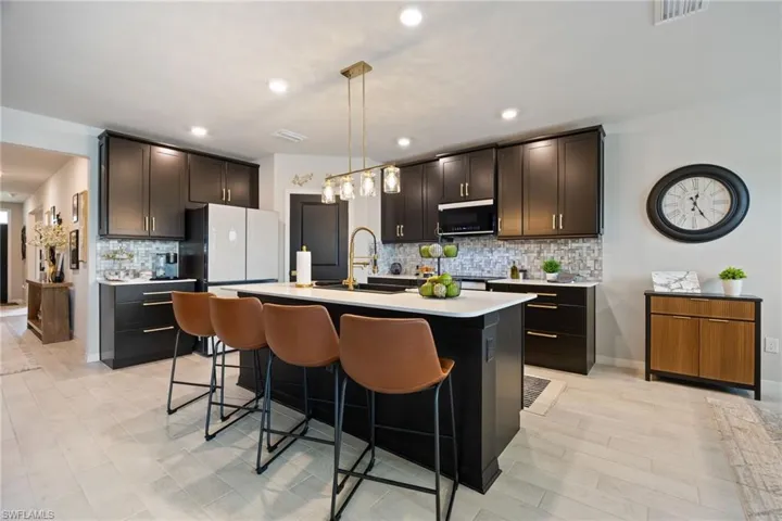 Kitchen with backsplash, hanging light fixtures, a kitchen breakfast bar, a kitchen island with sink, and recessed lighting