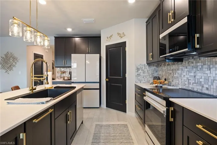 Kitchen with stainless steel appliances, backsplash, dark cabinets, decorative light fixtures, and light stone counters