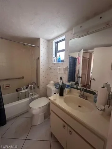 Bathroom with a textured ceiling, toilet, shower / tub combo, vanity, and tile patterned floors