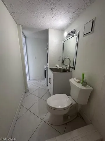 Bathroom with a textured ceiling, toilet, vanity, baseboards, and stacked washing maching and dryer