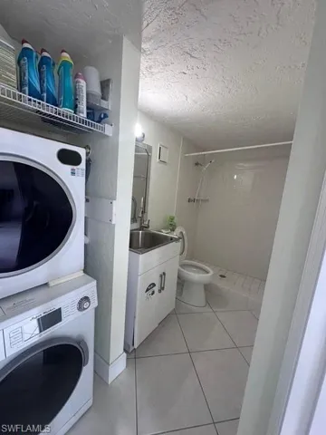 Full bath featuring a textured ceiling, toilet, stacked washer and dryer, vanity, and a stall shower