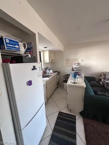 Kitchen featuring white appliances, light tile patterned floors, light countertops, under cabinet range hood, and a sink
