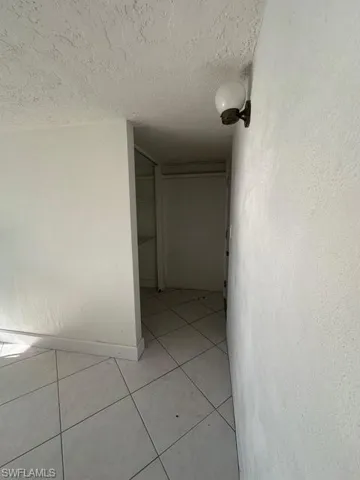 Hall featuring a textured ceiling, a textured wall, light tile patterned flooring, and baseboards