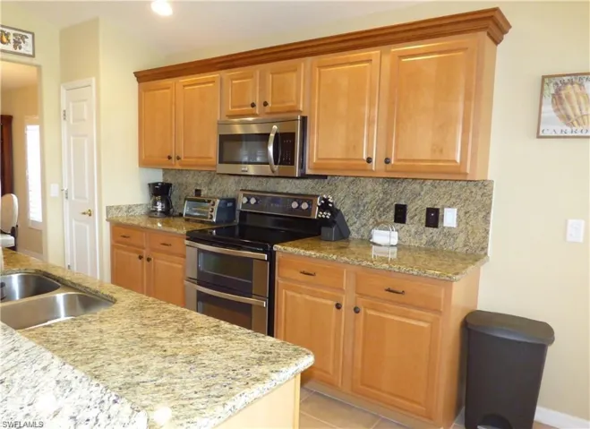 Kitchen featuring light tile patterned flooring, tasteful backsplash, light stone counters, and electric stove