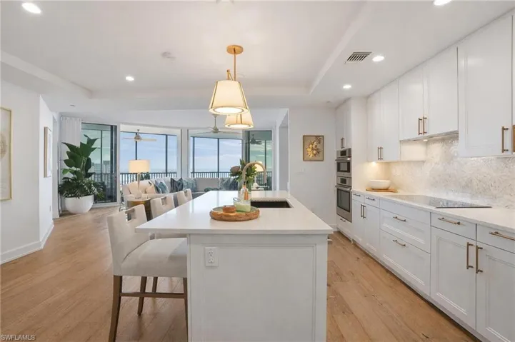 Kitchen featuring white cabinetry, open floor plan, pendant lighting, a center island with sink, and a breakfast bar area - Virtually Edited Image