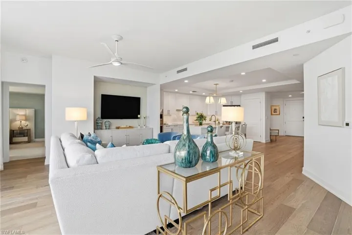 Living area featuring a tray ceiling, light wood-type flooring, recessed lighting, a ceiling fan, and a chandelier - Virtually Edited Image