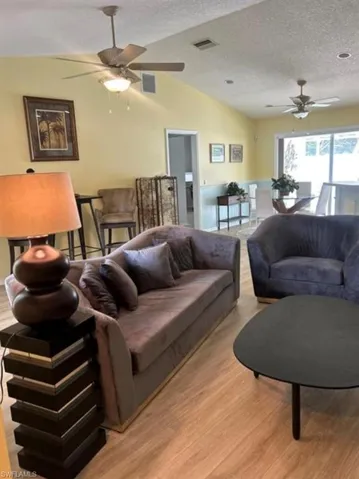 Living room with a ceiling fan, vaulted ceiling, light wood finished floors, and a textured ceiling