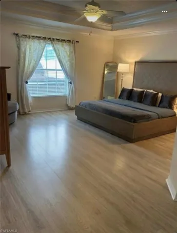 Large light filled bedroom  featuring crown molding, ceiling fan, light wood-style floors, and a tray ceiling
