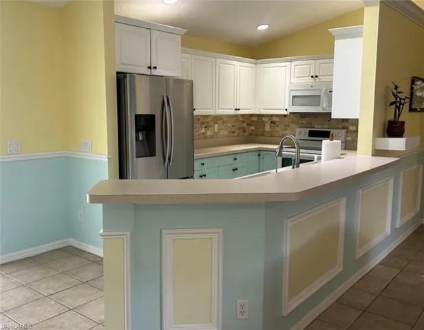 Kitchen with tile flooring and stainless steel appliances, white cabinetry, and vaulted ceiling