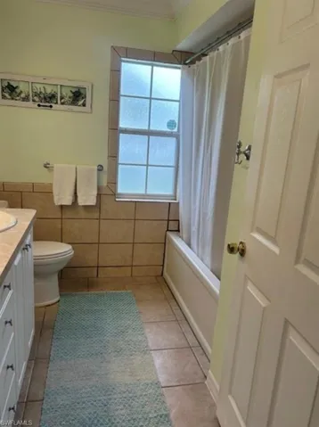 Full bathroom with vanity, light tile patterned floors, shower / bath combination with curtain, crown molding, and tile walls