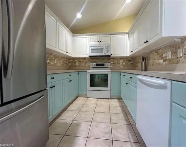 Kitchen featuring white cabinetry, lofted ceiling, light tile patterned floors, and backsplash