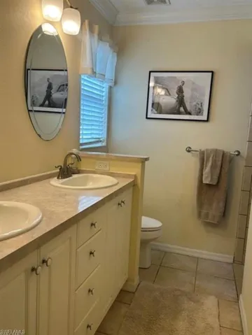 Full bath featuring double vanity, ornamental molding, and light tile patterned flooring