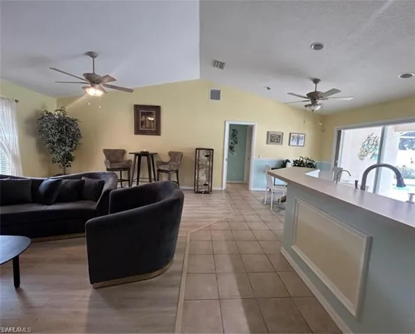 Living area with a ceiling fan, plenty of natural light, vaulted ceiling, a textured ceiling, and light tile patterned floors