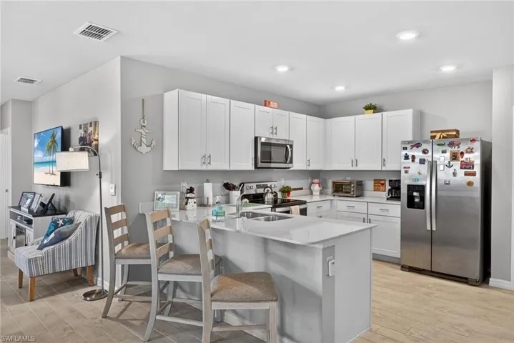 Kitchen with stainless steel appliances, a peninsula, tile floors, white cabinetry, and recessed lighting