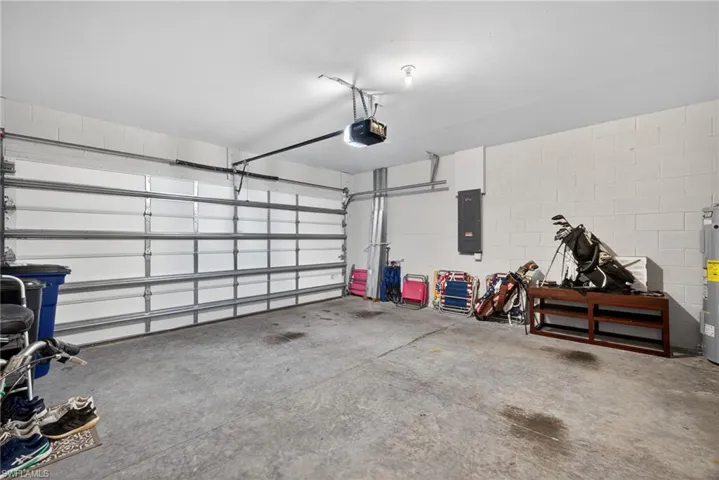 Garage featuring electric panel, concrete block wall, electric water heater, and a garage door opener