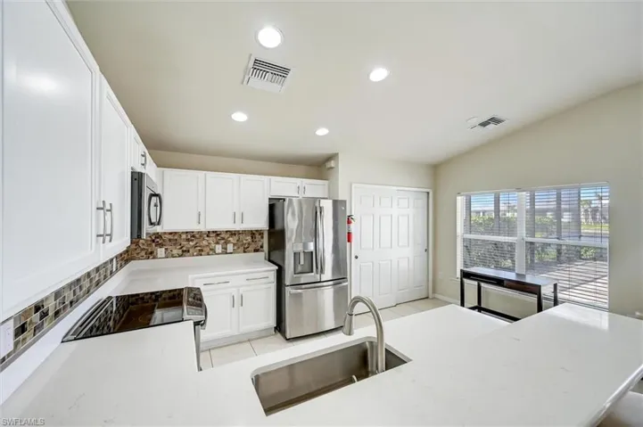 Kitchen with white cabinets, backsplash, stainless steel appliances, recessed lighting, and vaulted ceiling