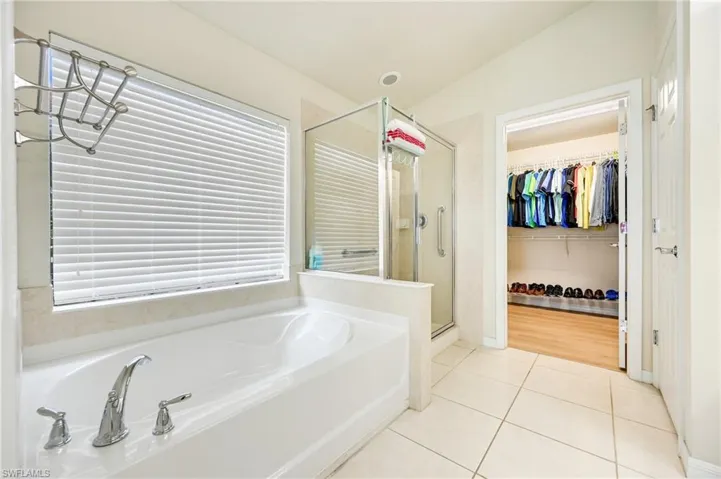Bathroom with a shower stall, a spacious closet, a bath, light tile patterned floors, and lofted ceiling