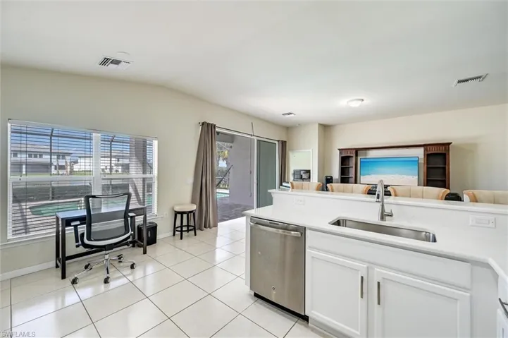 Kitchen featuring stainless steel dishwasher, white cabinets, light tile patterned floors, vaulted ceiling, and open floor plan