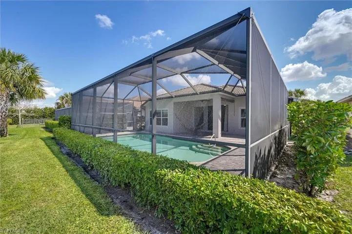 Rear view of property featuring a sunroom, an outdoor pool, a lawn, glass enclosure, and stucco siding