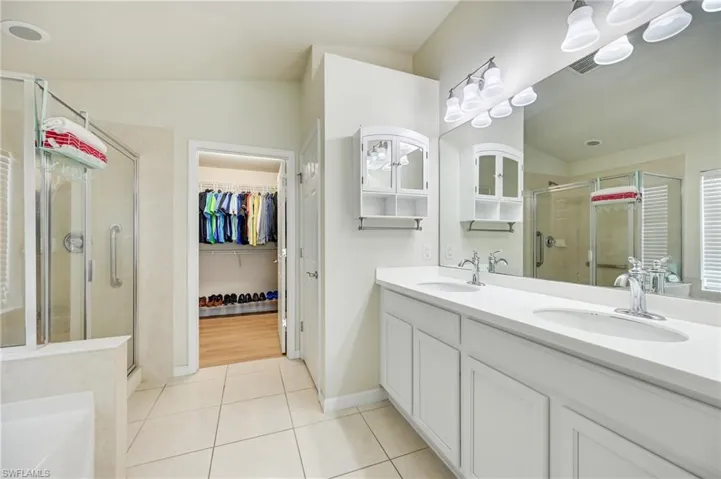 Full bath with double vanity, a shower stall, a garden tub, a spacious closet, and light tile patterned floors
