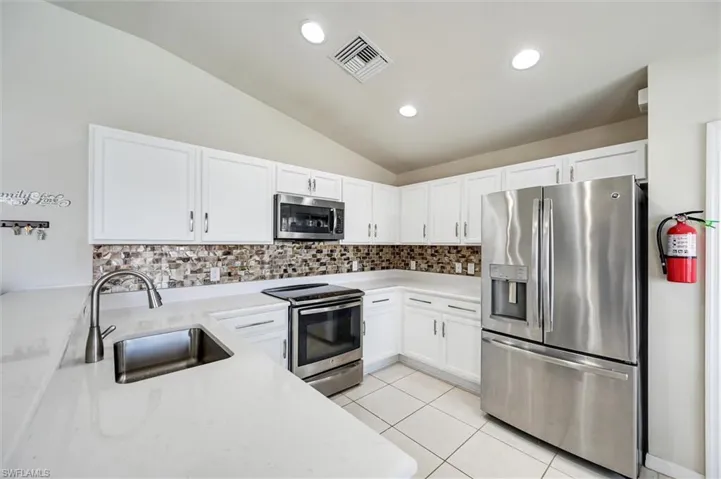 Kitchen with stainless steel appliances, vaulted ceiling, white cabinets, tasteful backsplash, and recessed lighting