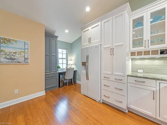 Kitchen featuring white fridge with ice dispenser, lofted ceiling, white cabinetry, and light wood-type flooring