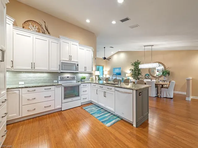 Kitchen with vaulted ceiling, light hardwood / wood-style floors, sink, kitchen peninsula, and white appliances