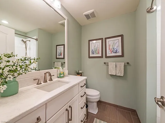 Bathroom with tiled shower, tile patterned flooring, toilet, and vanity