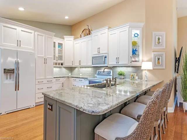 Kitchen with white cabinets, light hardwood / wood-style floors, decorative backsplash, and white refrigerator with ice dispenser