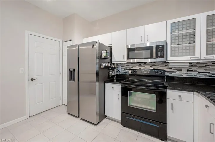 Kitchen with backsplash, white cabinetry, light tile patterned floors, and stainless steel appliances