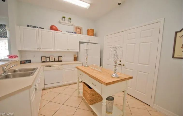 Kitchen featuring white cabinets, light tile patterned floors, sink, white appliances, and a center island