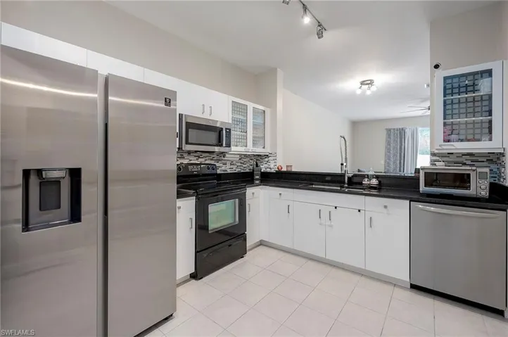 Kitchen with appliances with stainless steel finishes, decorative backsplash, white cabinetry, light tile patterned floors, and sink