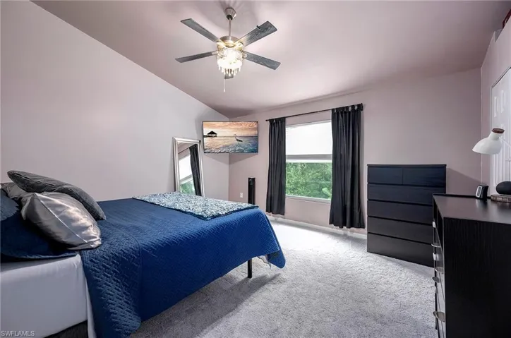 Carpeted bedroom featuring ceiling fan and vaulted ceiling