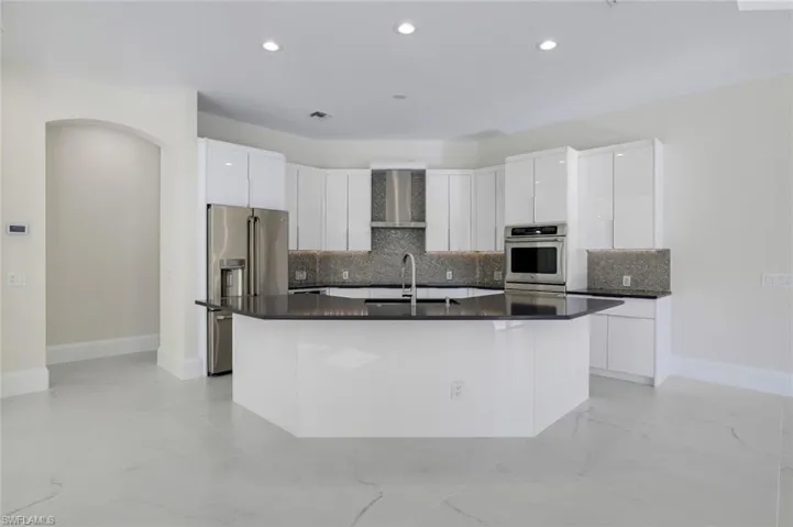 Kitchen with appliances with stainless steel finishes, wall chimney exhaust hood, an island with sink, and white cabinets