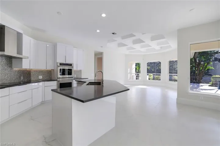 Kitchen featuring wall chimney range hood, sink, double oven, white cabinets, and a center island with sink
